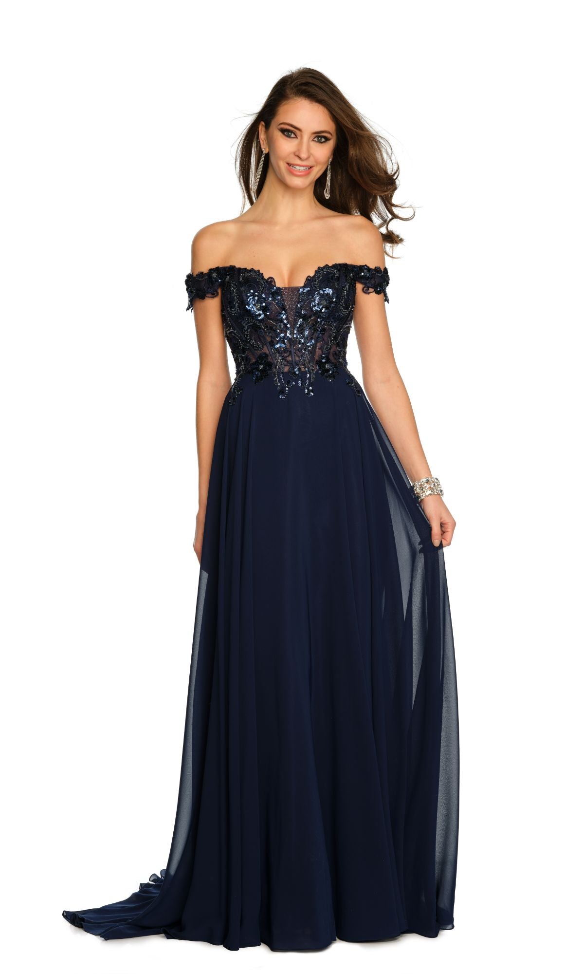 A woman stands smiling at the camera in the Dave and Johnny Off-Shoulder Navy Prom Dress 11242, featuring a sequined bodice and a flowing skirt.